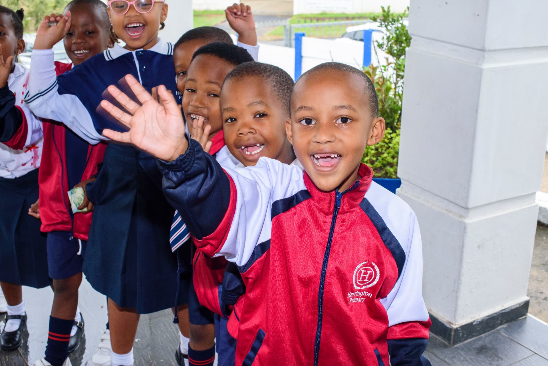 A group of Harrington Primary School pupils waving and smiling outdoors