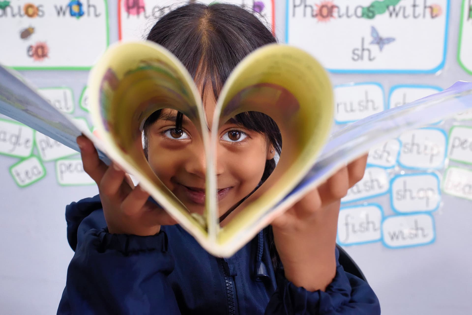 A young pupil holding an open book in the shape of a heart